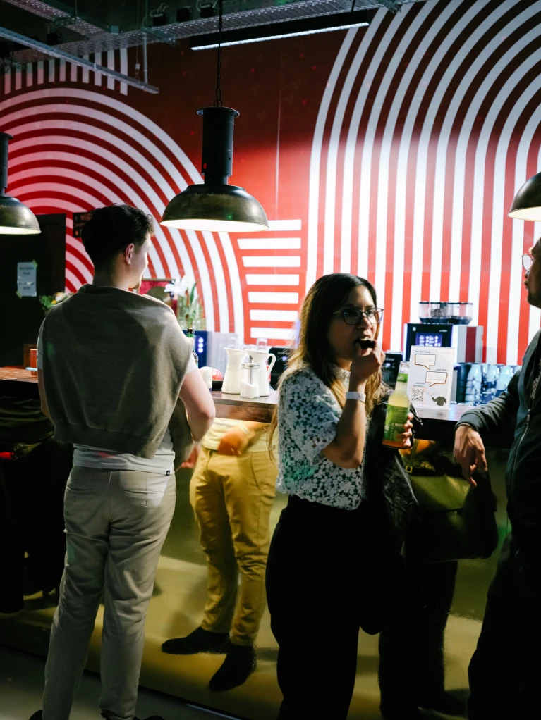 Menschen unterhalten sich in einer stilvollen Bar mit auffälliger rot-weißer Spiralenwanddekoration und industriellen Hängelampen