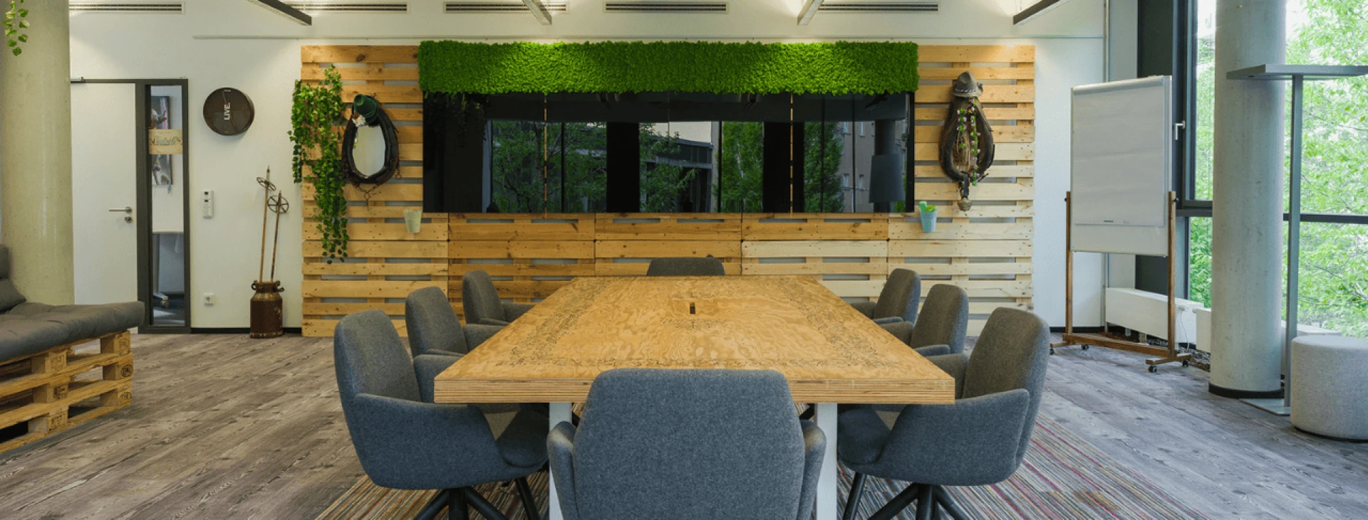 Moderner Besprechungsraum mit großem Holztisch, umgeben von grauen Stühlen, Holzverkleidung und grüner Wanddekoration