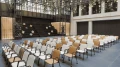 Interior of a modern venue featuring multiple rows of beige and black chairs facing a black staircase with geometric gold decorations on the wall