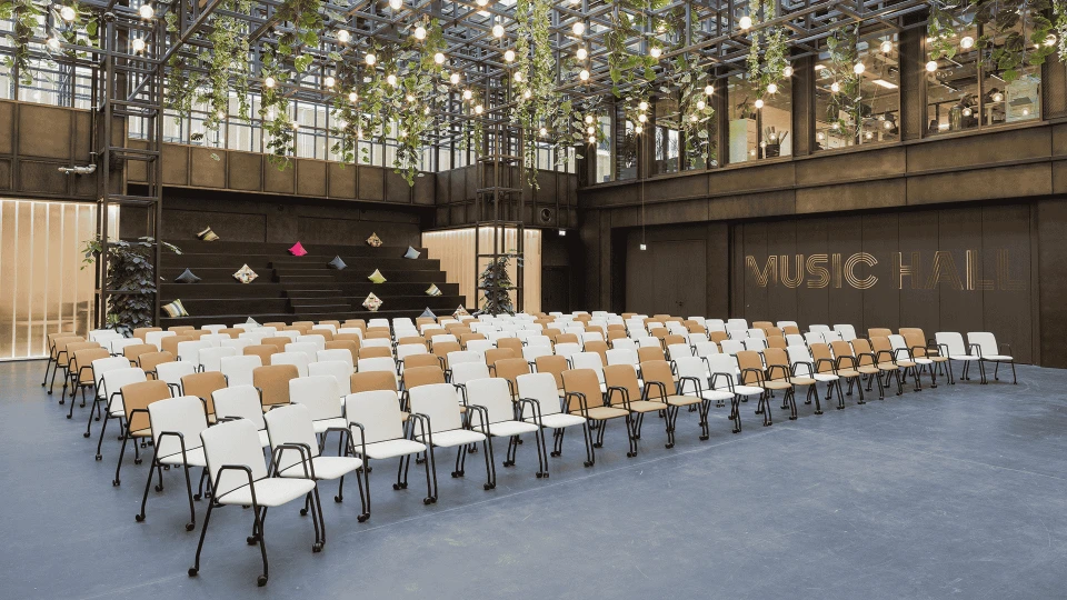 Modern event hall with rows of white chairs, a stage with geometric shapes, and an illuminated 'FUSION HALL' sign