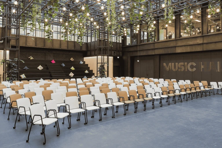 Moderne Veranstaltungshalle mit Reihen aus weißen Stühlen, einer Bühne mit geometrischen Formen und beleuchtetem 'FUSION HALL'-Schriftzug