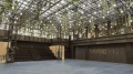 Modern hall with a glass roof through which plants hang, illuminated by numerous bulbs, featuring a large staircase and the inscription 'WERK STATT' on a wall.