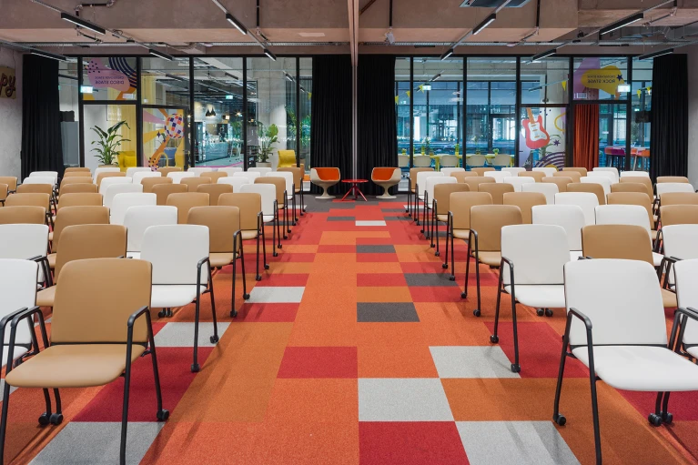 Blick durch die Crossover Stage im Smartvillage B-NK mit bunter Teppichgestaltung und Stuhlreihen