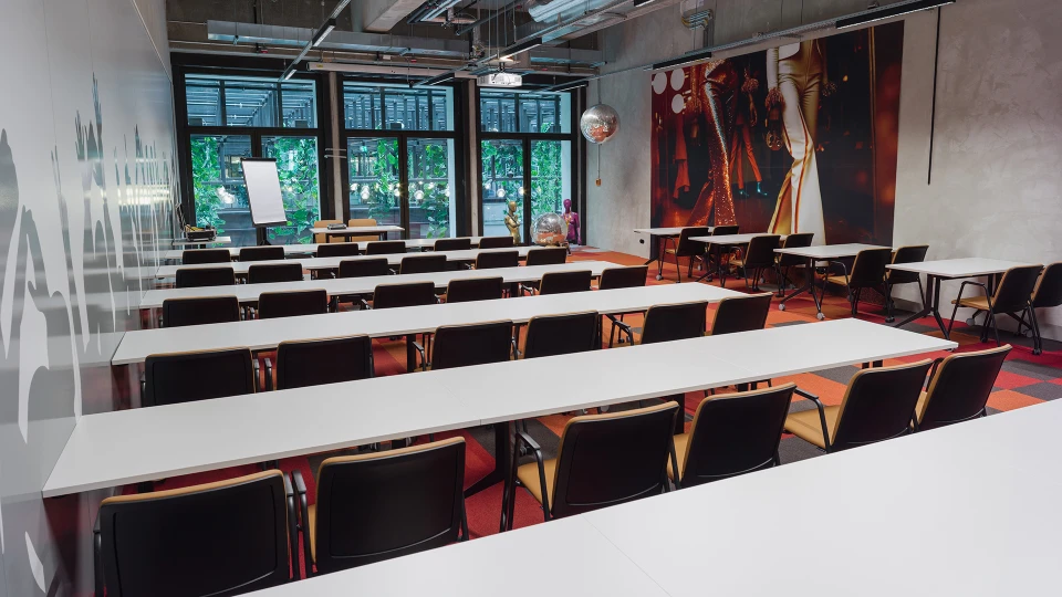 Innenansicht des Disco Stage Raumes mit Fokus auf die Bestuhlung und die grüne Fassadenbegrünung im Hintergrund, Wandgrafik mit feiernder Menschenmenge.
