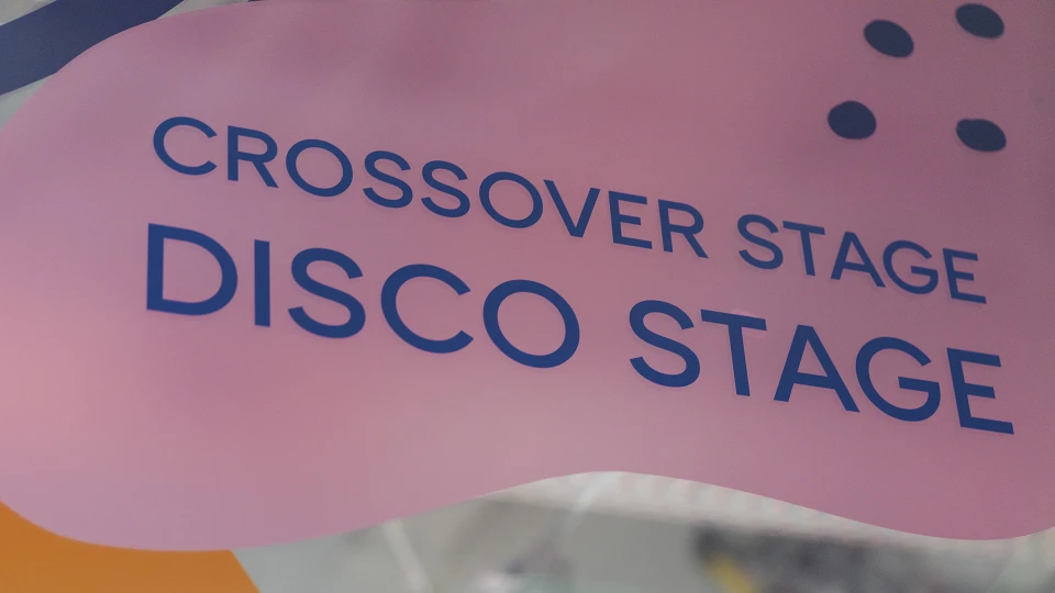 Nahaufnahme des pinken Türschildes mit der Aufschrift „Crossover Stage Disco Stage“.