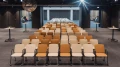 Moderne Konferenzsaal mit Reihen von orangen und beigen Stühlen gerichtet auf eine Bühne im Hintergrund, beleuchtet von Deckenspots.