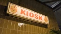 Vintage-Leuchtschild mit der Aufschrift „KIOSK“ und Hirschner Pilsener Logos, montiert an einer Wand mit grünen Keramikfliesen.