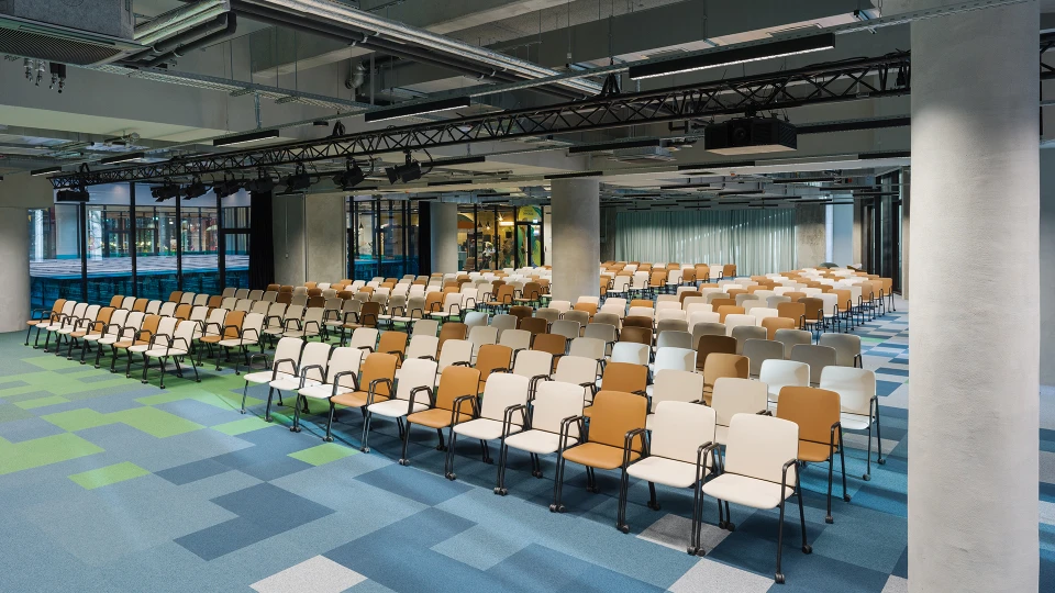 Blick auf die bestuhlte Eventfläche mit Sicht auf moderne Deckenkonstruktion mit Lichttechnik und abgehängten Elementen.