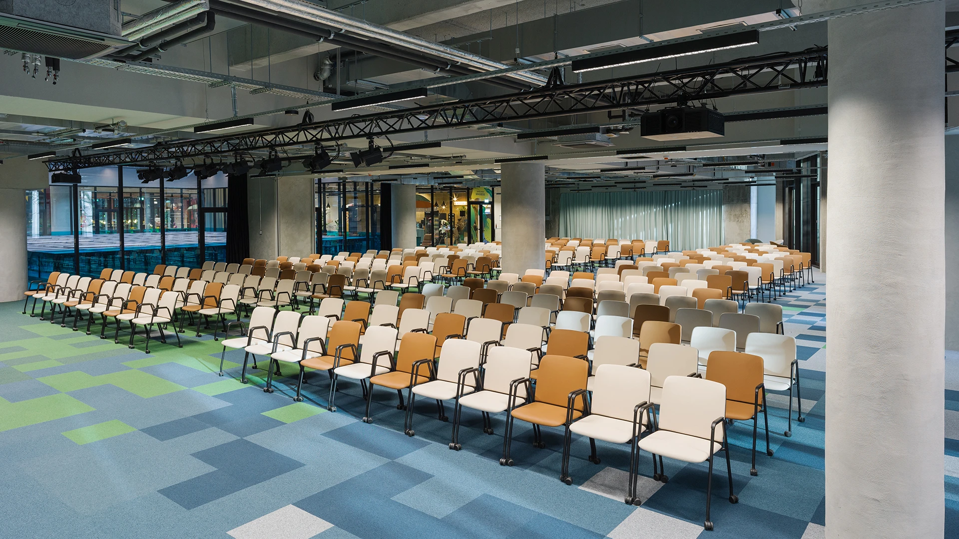 Blick auf die bestuhlte Eventfläche mit Sicht auf moderne Deckenkonstruktion mit Lichttechnik und abgehängten Elementen.