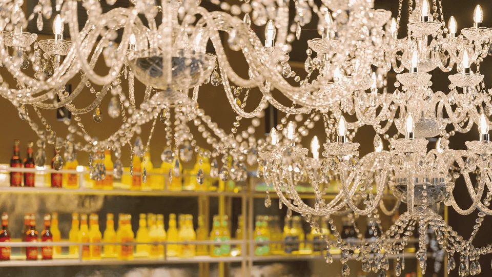 Luxuriöse Kristallkronleuchter vor einem unscharfen Hintergrund einer Bar mit beleuchteten Spirituosenregalen.