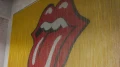 Meetingraum mit auffälliger Rolling-Stones-Zunge als Kettenvorhang auf gelbem Hintergrund, U-förmig gestellte Tische und bunte Teppichfliesen.
