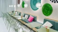 View of a cozy seating area with green folding chairs and light green tables in front of a wall adorned with circular graphic artworks and moss installations.