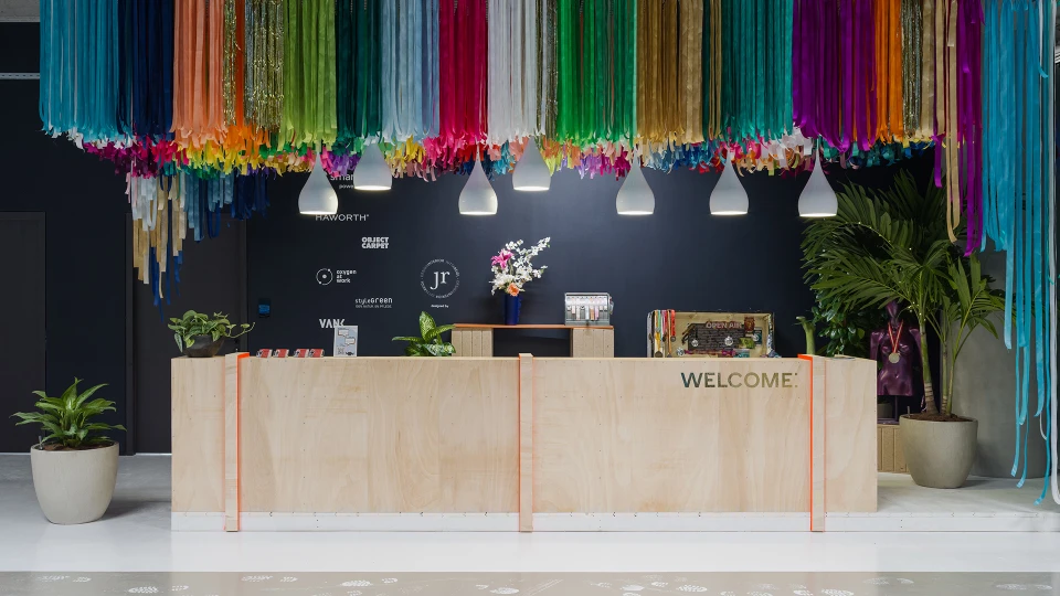 Empfangstresen mit großem „WELCOME“-Schriftzug und bunter Stoffdeko an der Decke.