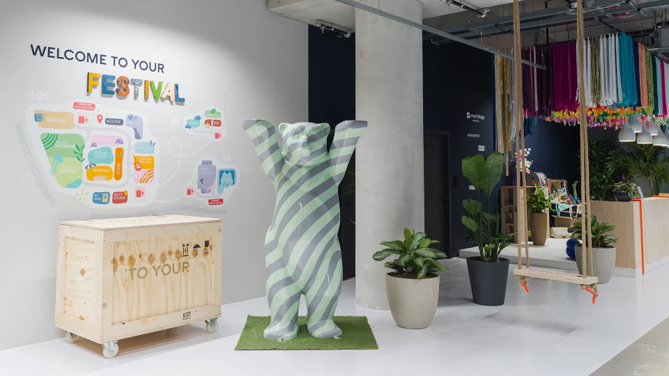 Breiter Flur mit Sitzgruppen, Pflanzen, farbenfroher Deckendeko und einem Empfangstresen auf der rechten Seite.