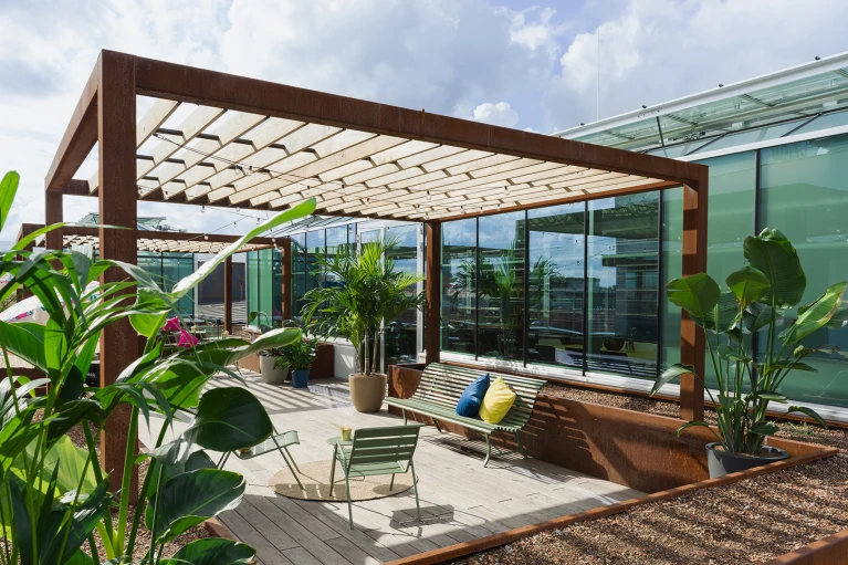 Moderne Dachterrasse mit hölzernem Pergola, eingebettet in üppige Pflanzen, mit Blick auf umliegende Gebäude.