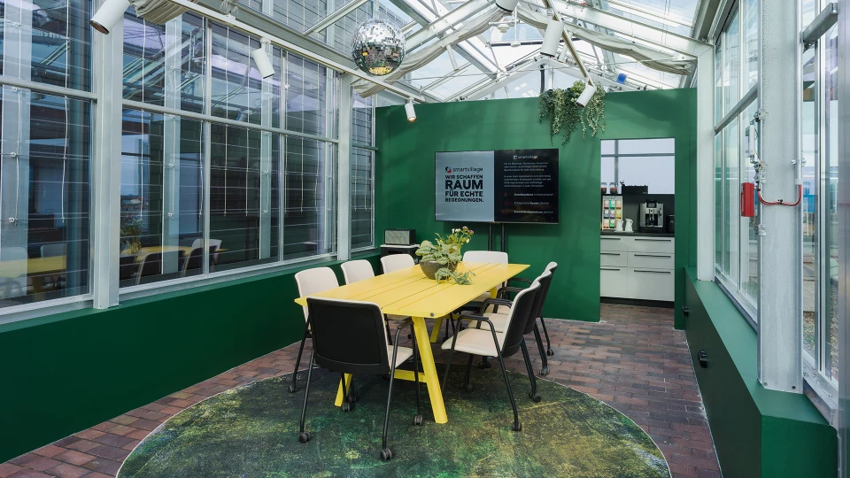 Heller, modern gestalteter Wintergarten mit grünen Wänden und Glasdach, eingerichtet mit einem gelben Tisch, schwarzen Stühlen und dekorativen Pflanzen.