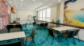 Heller Meetingraum mit türkisfarbenem Teppich, weißen Tischen und grauen Stühlen. Die Wand ist mit einem großen Strandmotiv sowie bunten Girlanden dekoriert, die eine kreative Atmosphäre schaffen