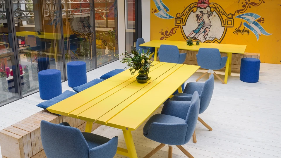 Detailansicht gelber Besprechungstisch mit blauen Stühlen und Wandkunst im Smartvillage Köln Mülheim