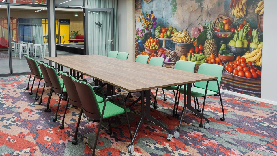 Konferenzraum Kolumbien Bogota mit großem Holztisch, grünen Stühlen und Wandbild eines Obst- und Gemüsemarkts, Blick auf Uruguay-Bereich im Smartvillage