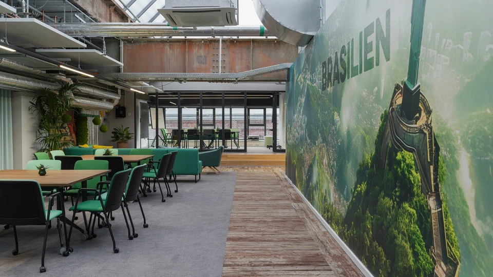 Gemütlicher Wartebereich im Brasilien-Raum des Smartvillage Köln-Mülheim mit hellblauen Sitzmöbeln, Bambusdeko und Glasfront