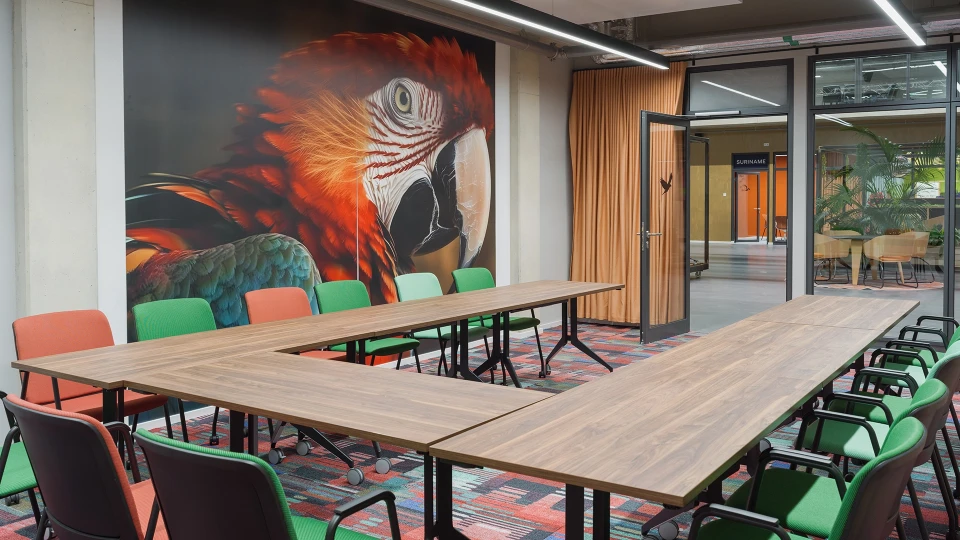 U-förmige Tischanordnung in einem farbenfrohen Besprechungsraum mit Papageien-Wandmotiv im Smartvillage Köln-Mülheim.