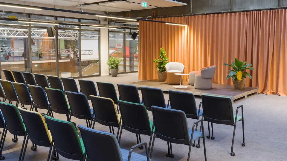 Seitenansicht der Bühne mit zwei gemütlichen Sesseln, einem kleinen Tisch und Pflanzen im Hintergrund, perfekt für Talks oder Paneldiskussionen.