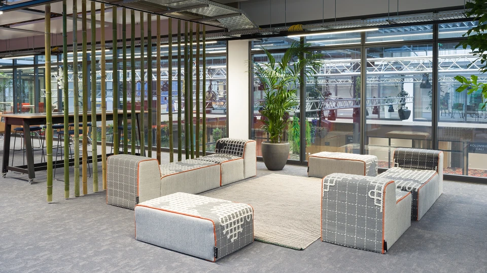 Gemütlicher Loungebereich mit modularen Sitzmöbeln, grüner Pflanzenwand und Bambus-Trennwänden.