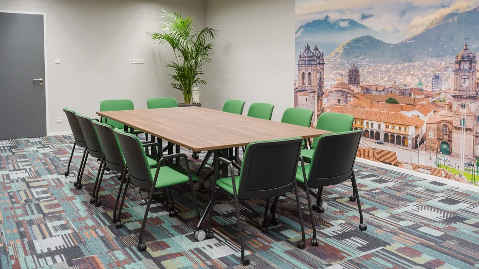 Konferenzraum mit grün gepolsterten Stühlen um einen rechteckigen Tisch und Fototapete der Stadt Cusco im Hintergrund.