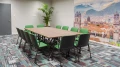 Konferenzraum mit grün gepolsterten Stühlen um einen rechteckigen Tisch und Fototapete der Stadt Cusco im Hintergrund.