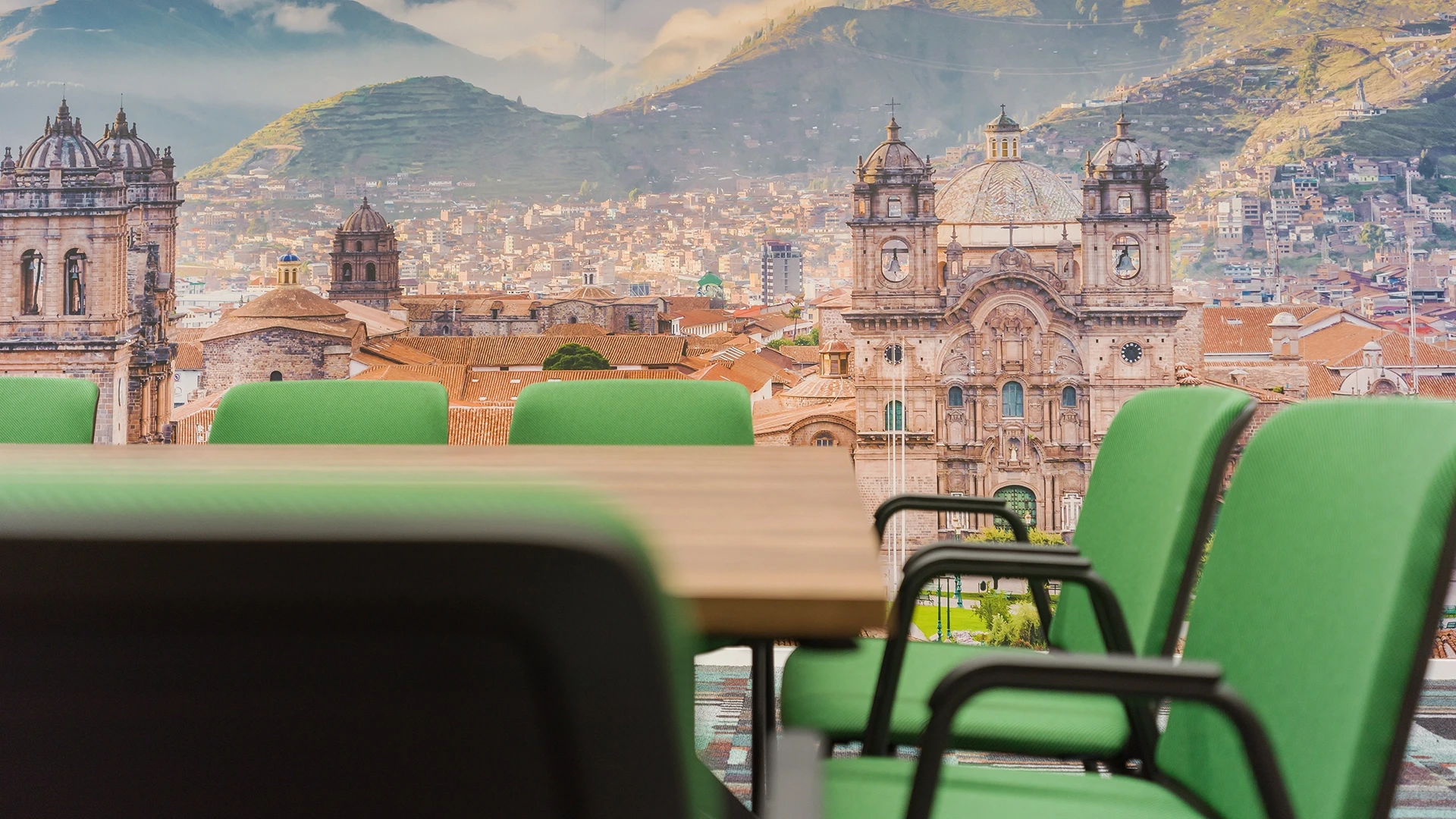 Nahaufnahme von grünen Stühlen im Raum Cusco mit Fokus auf die imposante Kirchenfassade von Cusco im Wandmotiv.