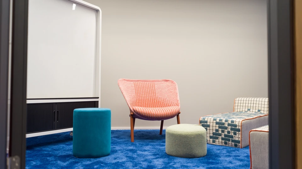 Blick in einen kleinen, modernen Meetingraum mit farbenfrohem Interieur und Whiteboard.