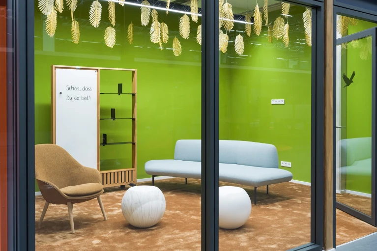 Innenansicht des Besprechungsraums "Guyana" mit grün gestrichener Wand, hellblauer Couch, braunem Sessel und weißen Kugelhockern.