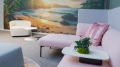 Moderner Loungebereich mit pastellfarbener Couch, weißen Beistelltischen und einer großen Wandgrafik mit tropischem Strandmotiv im Hintergrund.
