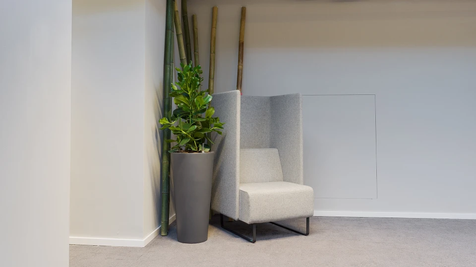 Rückzugsnische mit hellgrauem, hochlehnbarem Lounge-Sessel neben einem hohen Pflanztopf und Bambusdeko in einer Raumecke.