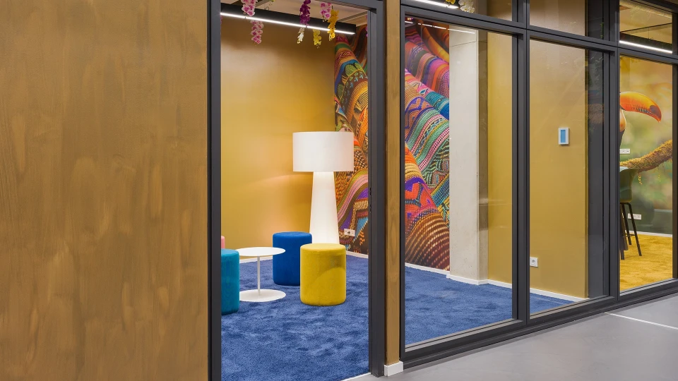 Außenansicht des Raums „Paraguay“ mit Glasfront und Blick auf Hocker, Stehlampe und Flipchart.