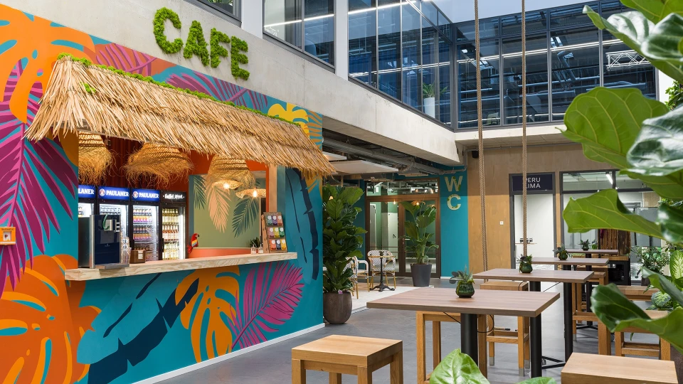 Blick auf die Theke des Smartcafés mit Strohdach, buntem Wandbild und Getränkekühlschränken.
