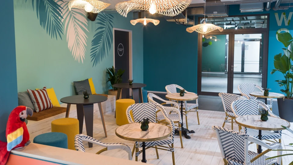 Außenansicht des Smartcafés mit hohem Sitzbereich und Blick auf das WC-Schild und die Tür zum Raum "Peru Lima".