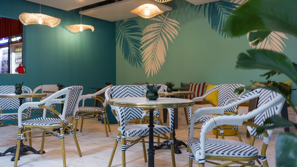 Frontalansicht des Sitzbereichs mit tropischer Tapete und Café-Tischen