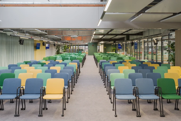 Zentralperspektive auf den farbenfroh bestuhlten Eventbereich mit Monitoren und Oberlichtern.