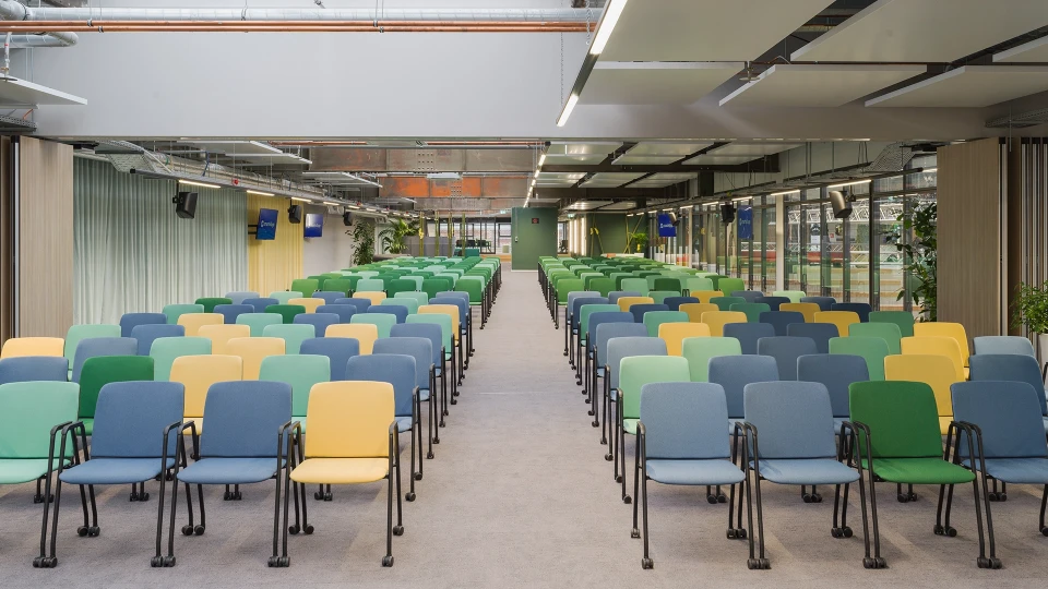 Zentralperspektive auf den farbenfroh bestuhlten Eventbereich mit Monitoren und Oberlichtern.