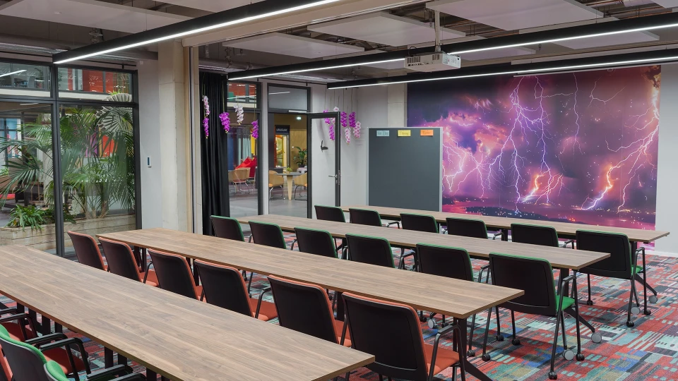 Moderner Besprechungsraum mit langem Tisch und Stühlen, farbenfrohem Teppich, großer Digitalanzeige mit Blitzdesign an der Wand und Pflanzen