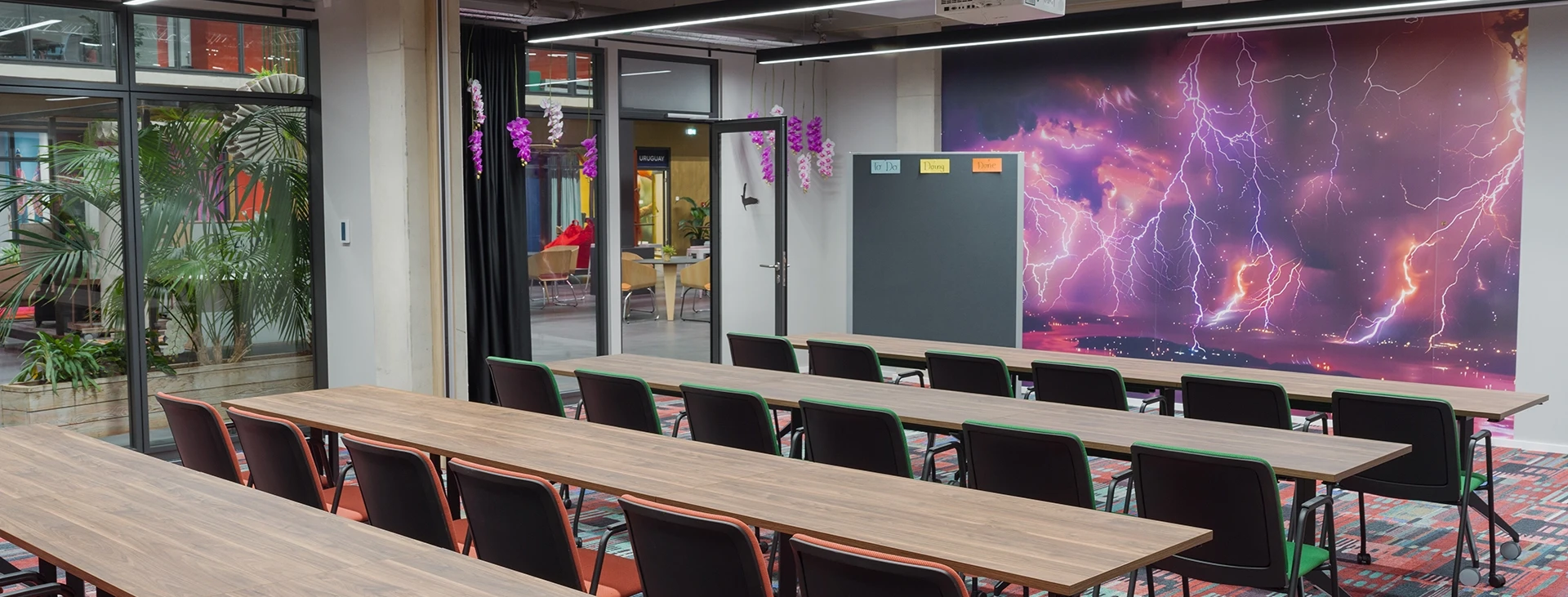 Moderner Besprechungsraum mit langem Tisch und Stühlen, farbenfrohem Teppich, großer Digitalanzeige mit Blitzdesign an der Wand und Pflanzen