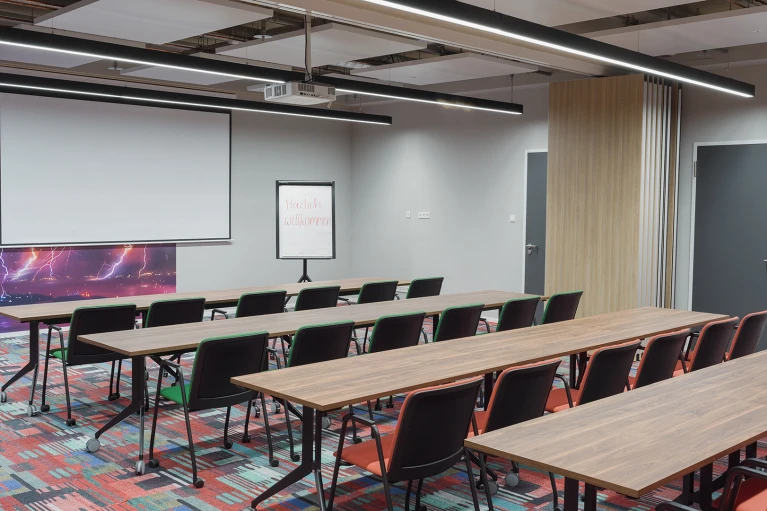 Moderne Konferenzraum mit langen Tischen und schwarzen Stühlen, eine weiße Leinwand an der Vorderseite und einer farbenfrohen Wand mit Weltraum-Motiv