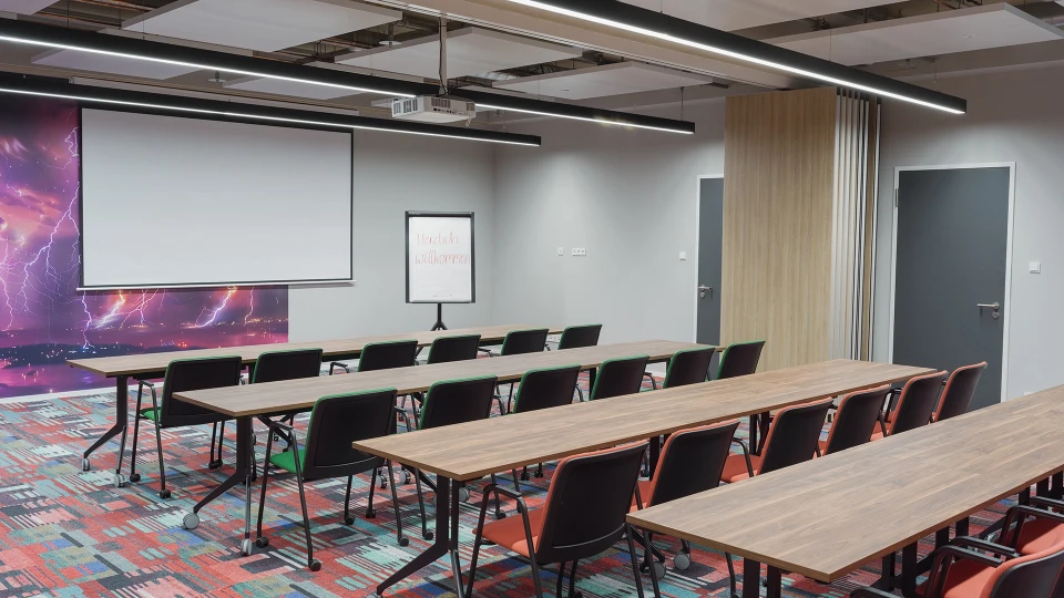 Moderne Konferenzraum mit langen Tischen und schwarzen Stühlen, eine weiße Leinwand an der Vorderseite und einer farbenfrohen Wand mit Weltraum-Motiv