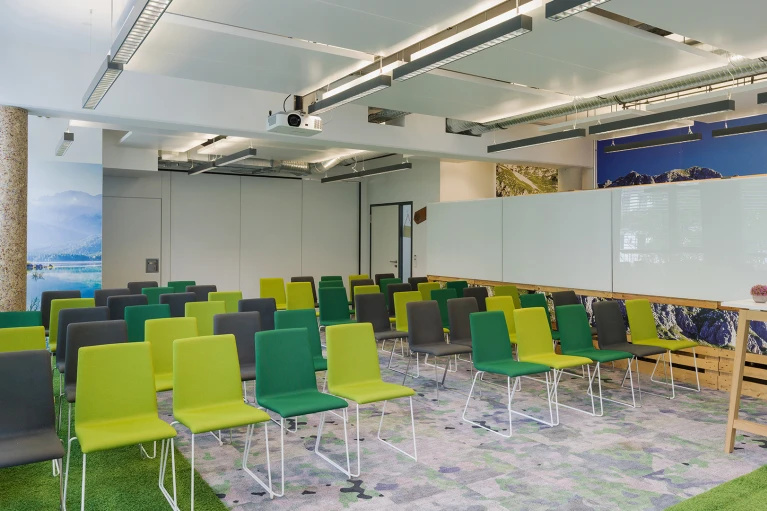 Modernes Seminarraum-Interieur mit grünen und gelben Stühlen, einem großen Bildschirm an der Wand und dekorativen Elementen
