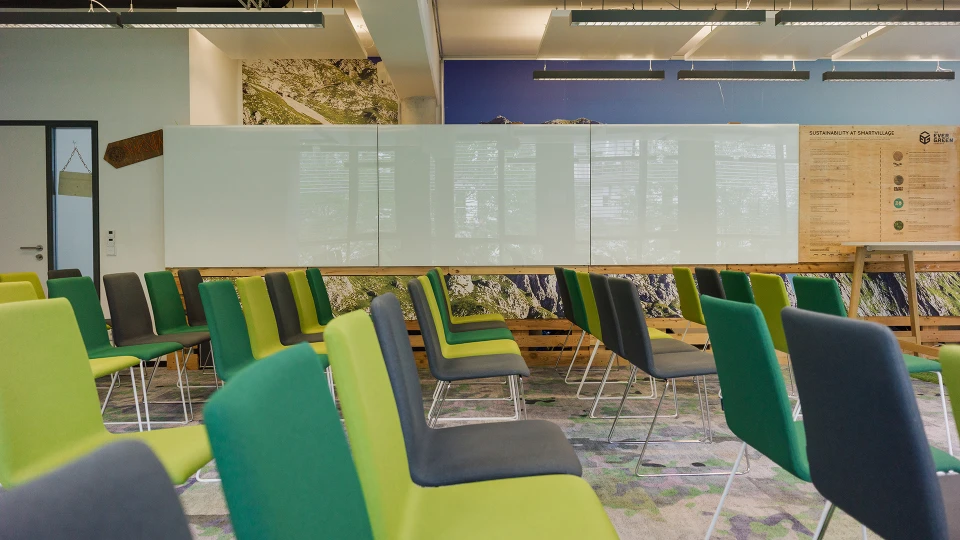 Moderne Büroumgebung mit grünen und grauen Stühlen um einen langen Holztisch, durchsichtige Trennwände mit Text, lebhafte Farbakzente und dynamische Beleuchtung.