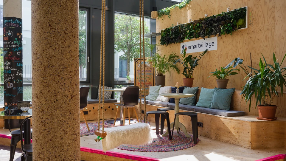 Modernes Büro-Lounge-Bereich mit natürlichen Holzmöbeln, Pflanzen und Schaukelseilen, gelegen in einem hell erleuchteten Raum mit großen Fenstern.