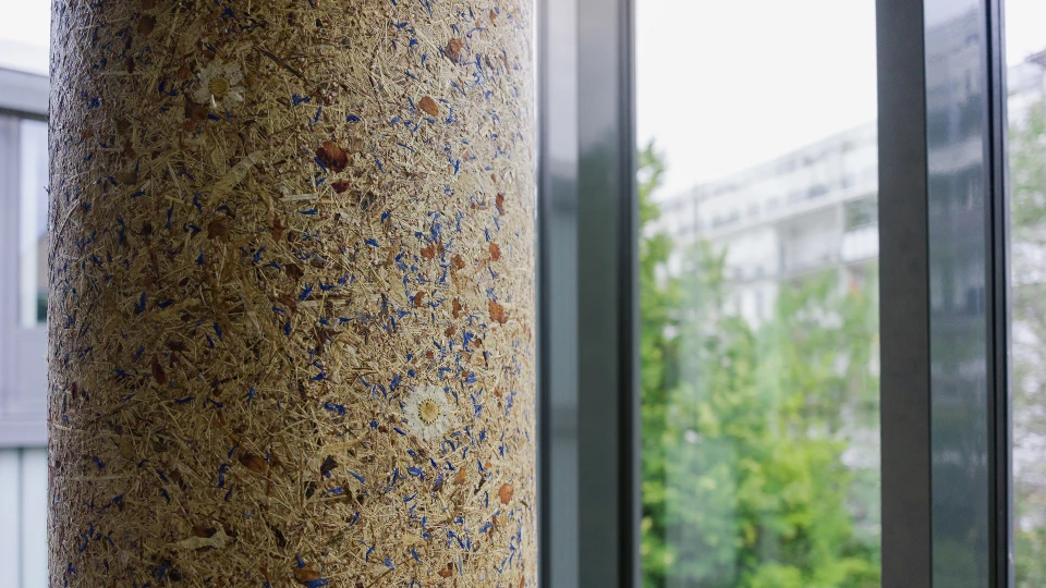 Nahaufnahme einer mit bunten Einschlüssen versehenen Korkoberfläche einer Säule vor einem Fenster mit Blick auf grüne Bäume