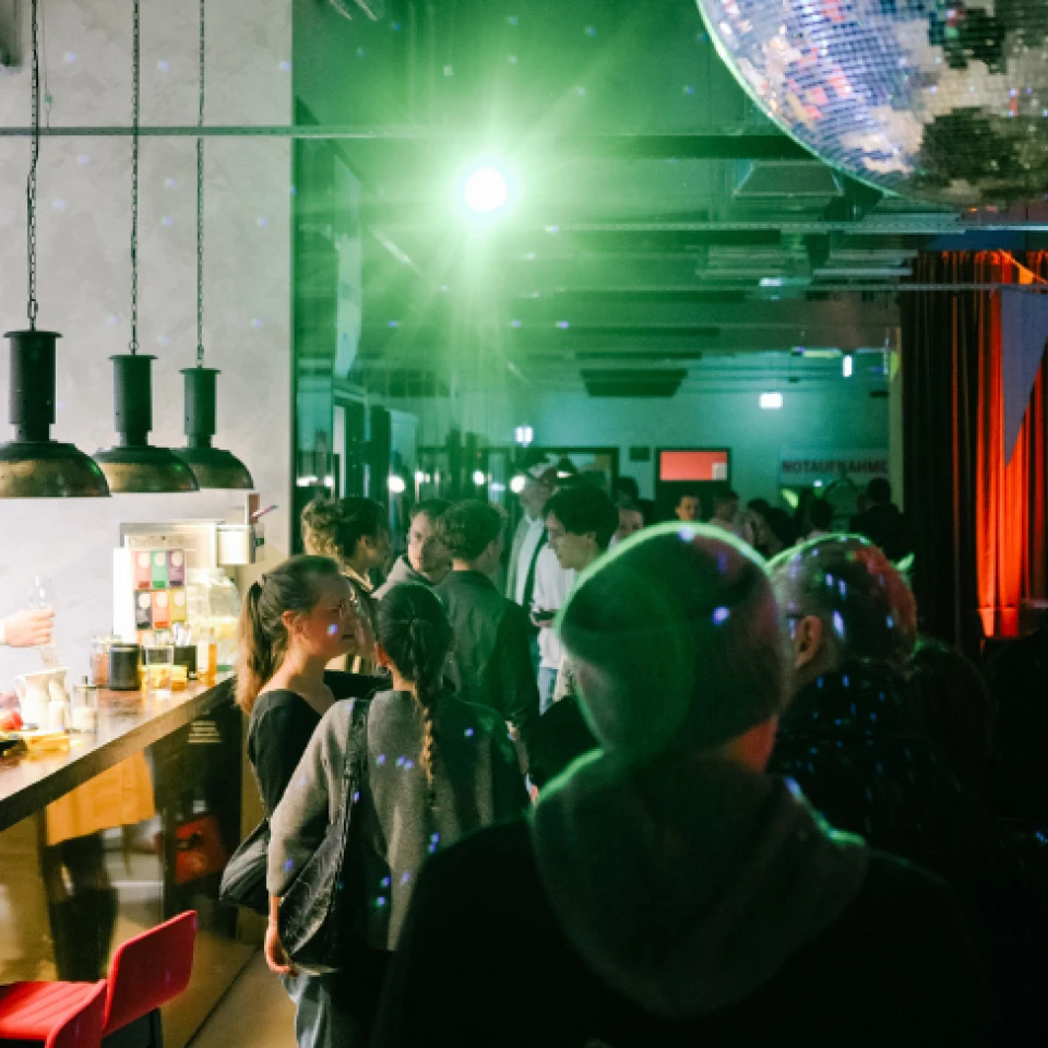 Lebendige Bar mit Menschen, die Getränke genießen, Barkeeper bei der Arbeit, beleuchtet durch bunte Lichter und eine große Diskokugel