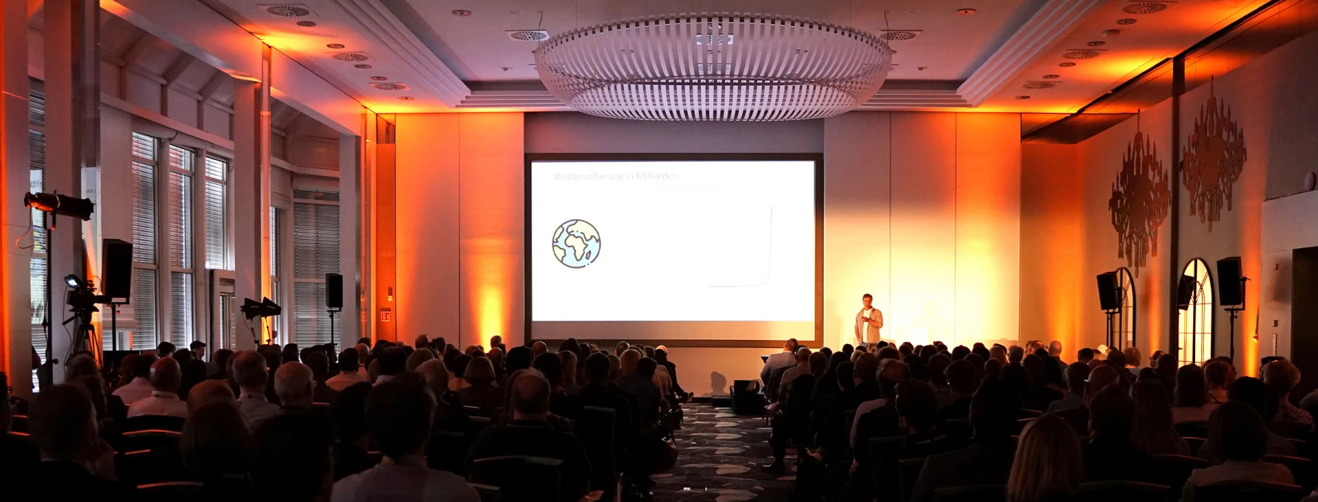 Eine Konferenzveranstaltung in einem großen Saal mit einer Person, die auf einer Bühne vor einem Bildschirm mit einer Gehirnillustration steht und vielen Zuhörern.